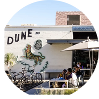 People sitting outside a building with 'DUNE' and a tiger mural on the wall.