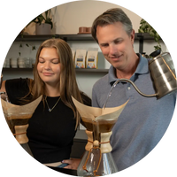 Two people brewing coffee with a Chemex coffee maker.