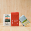  Two bags of coffee on either side of a red Trade bag that reads 