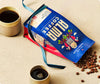  A coffee bag from Alma Coffee with a cup of coffee and coffee beans on a beige surface. 
