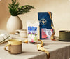  Two coffee bags from Alma Coffee and PT's Coffee Roasting Co on a table along with two mugs against a neutral background. 