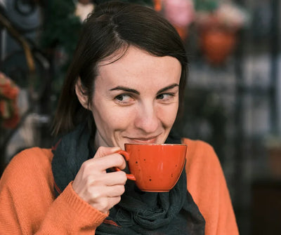 Woman in an orange sweater smiling while sipping espresso from a bright orange cup