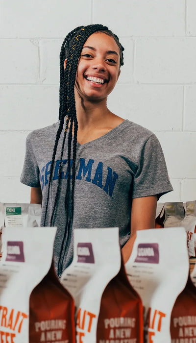 Smiling woman standing behind rows of coffee bags reading Pouring a New Narrative