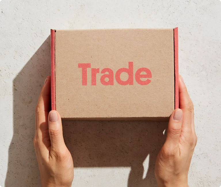 Brown cardboard box with 'Trade' printed on it held by hands against a light background