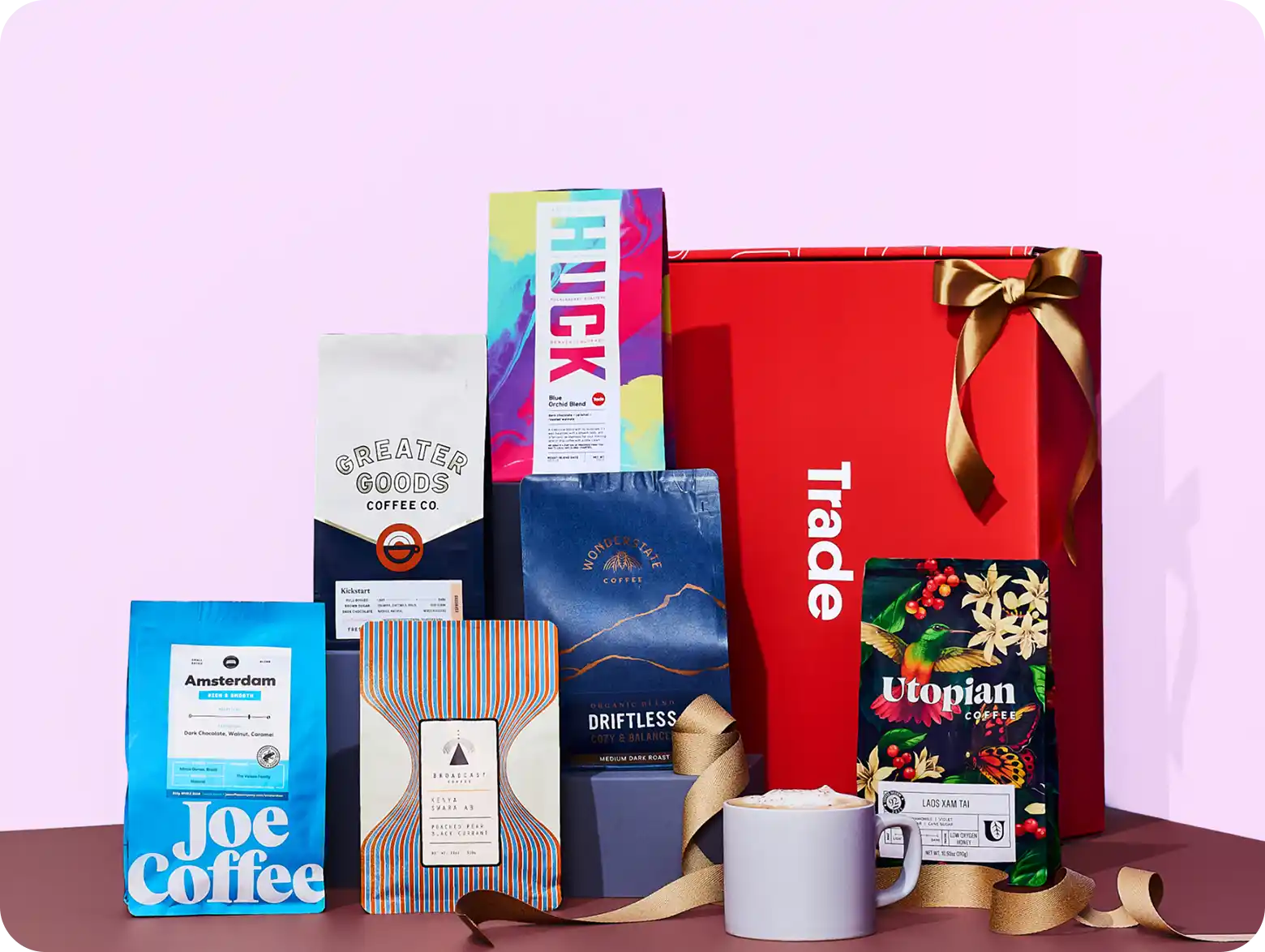 A variety of coffee bags from several different roasters along with a mug of coffee, all in front of a red Trade gift box.